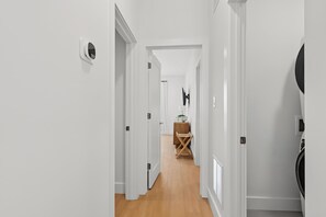 Passadís amb parets blanques, terra de fusta i una porta que dona a una habitació amb un llit i una televisió.