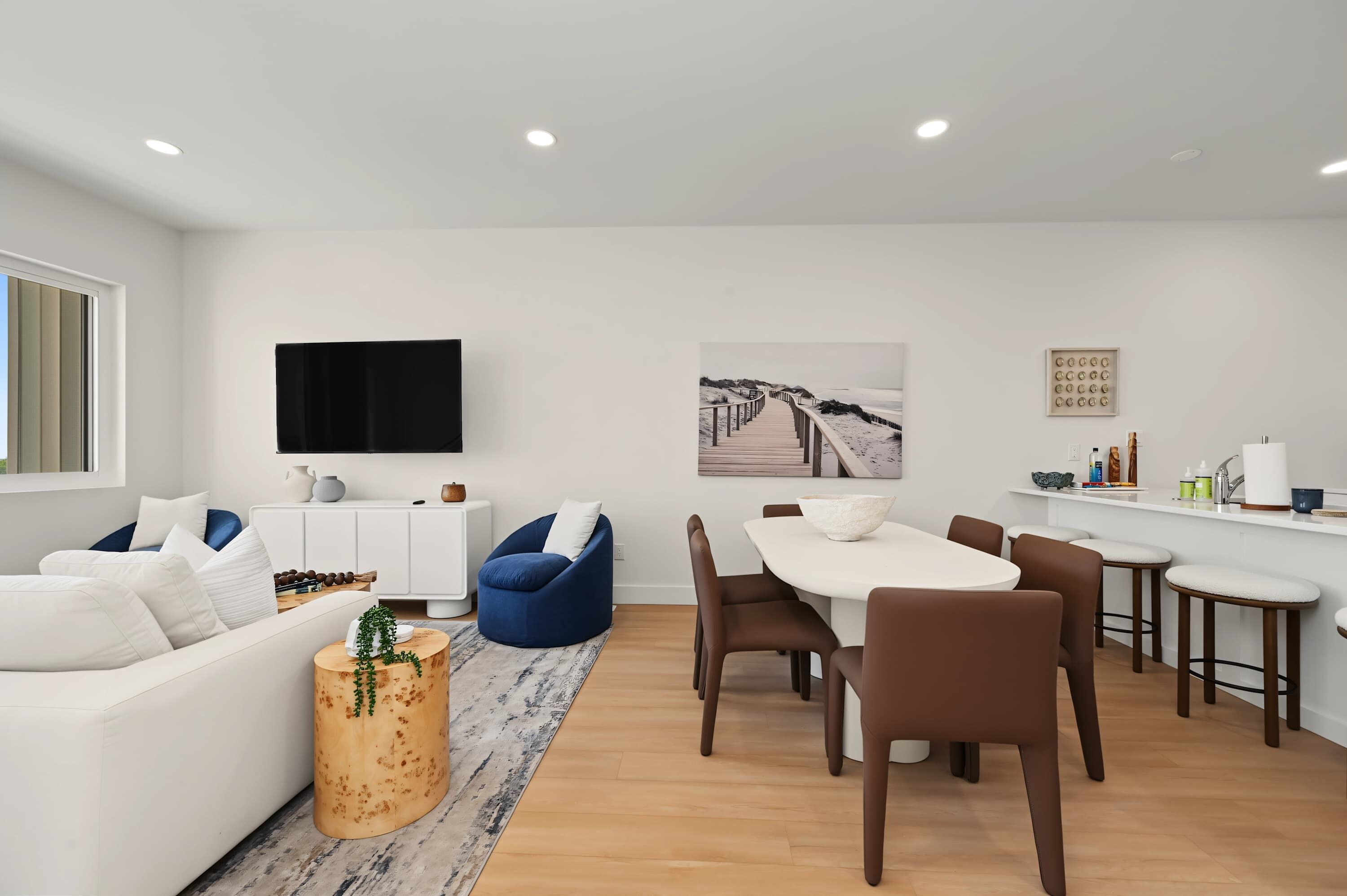 A modern living room with a white sofa, blue bean bag, and a dining area with a white table and brown chairs.