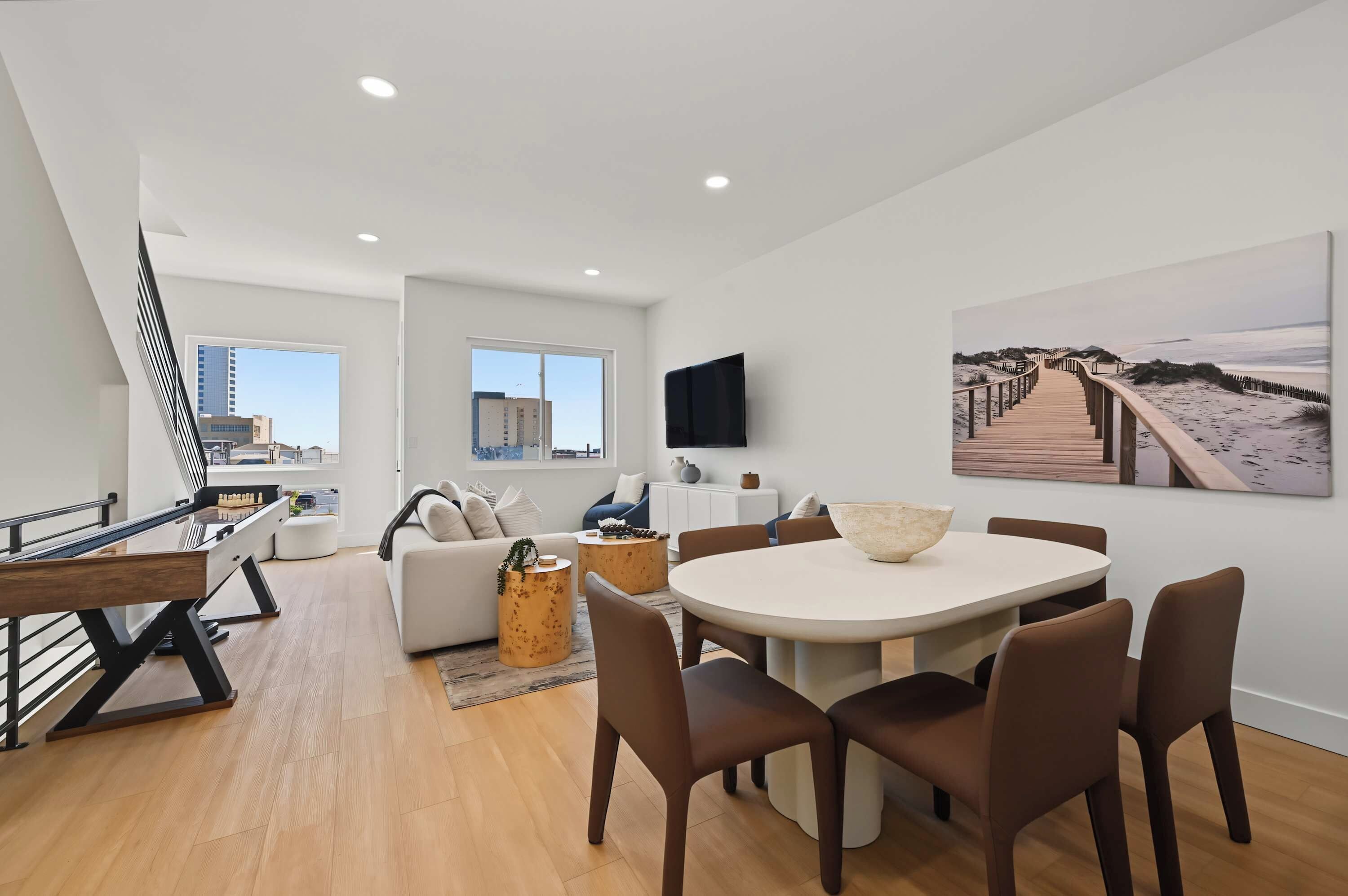A modern living space with a dining area, a sofa, a coffee table, and a painting of a beach walkway.