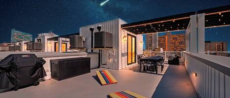 Une terrasse sur le toit offrant une vue dégagée sur le ciel nocturne, un espace repas et un jeu de société coloré à rayures.