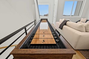 Ein schmales Brettspieltisch mit nummerierten Feldern, ein schwarzer Geländer und ein beiges Sofa in einem Raum mit weißen Wänden und Fenstern.