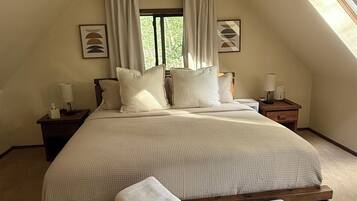 A bedroom with a large bed, a bedside table with a lamp, a bench, and a window with curtains.