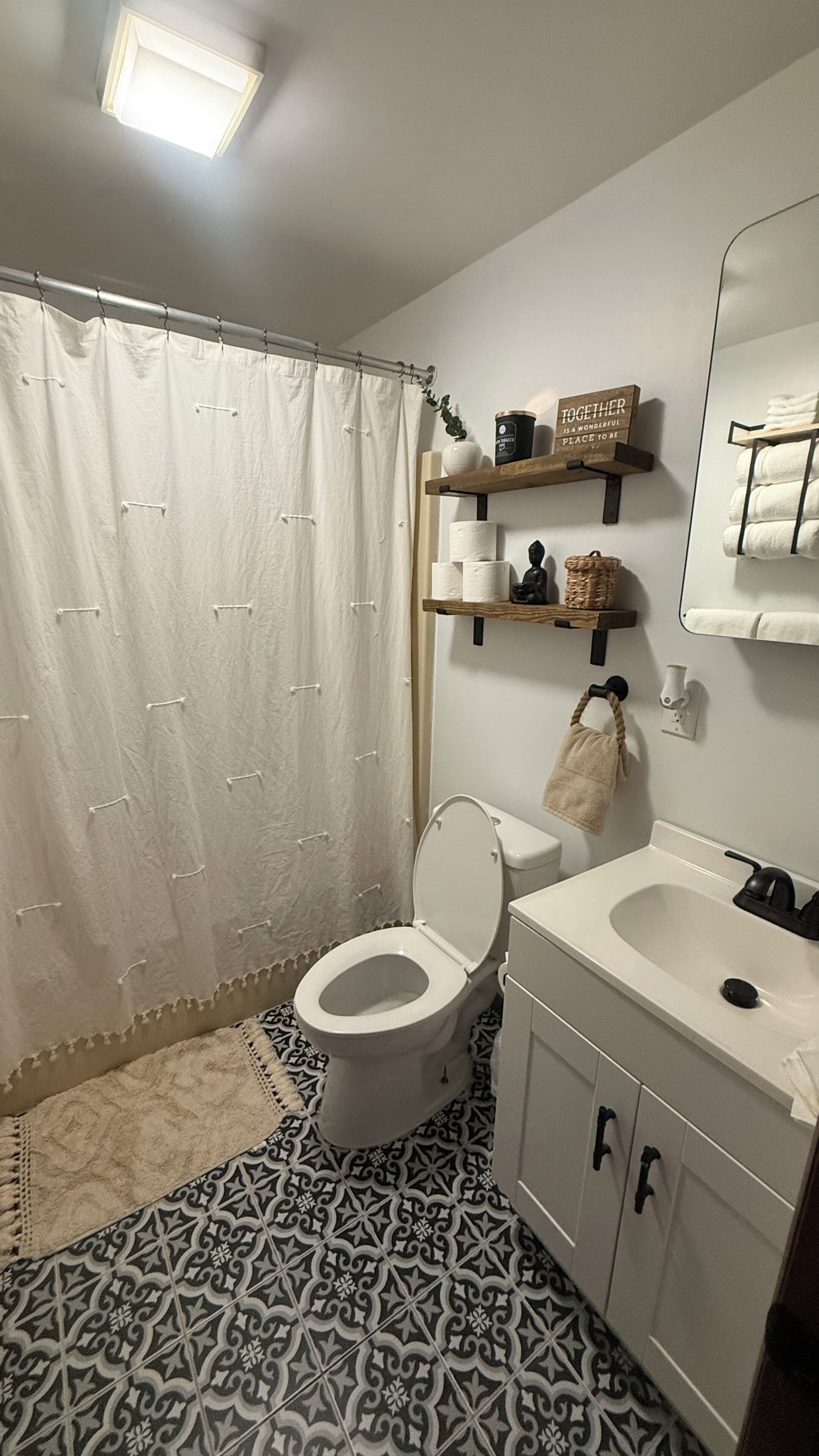 A bathroom with a toilet, sink, and shower curtain. There are shelves with toiletries and a towel rack.