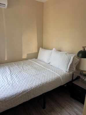 A single bed with a white duvet and pillows, a bedside table with a lamp, and a wooden floor.