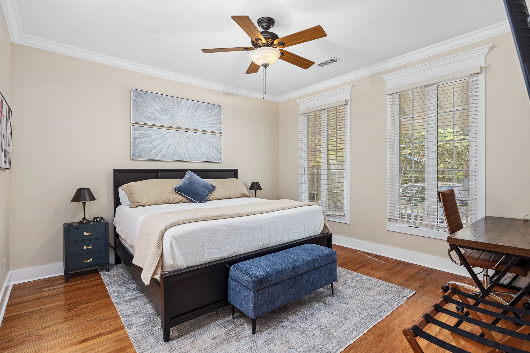 A bedroom with a bed, bedside tables, a desk, and a ceiling fan.