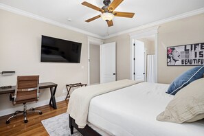 A bedroom with a bed, a desk, a chair, a ceiling fan, and a wall-mounted TV.