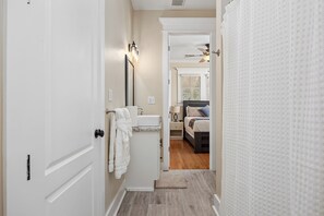 A hallway leading to a bedroom with a bed, a nightstand, and a bathroom with a sink and towel rack.