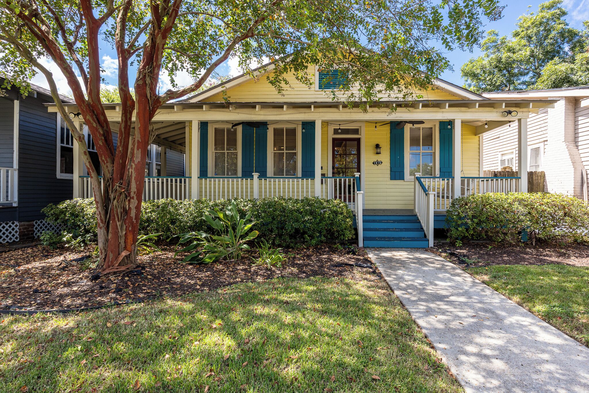 A house with a front porch, a tree, and a well-maintained lawn.