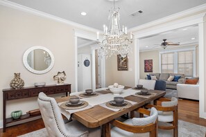 A dining area with a wooden table set for four, surrounded by chairs with white cushions. A chandelier hangs above the table, and a mirror is mounted on the wall. - Garden District Luxury Retreat!  Homebase for Sports, Work & Families! (Baton Rouge)
