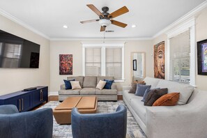 A living room with a ceiling fan, a sofa set, a coffee table, and a TV on the wall. - Garden District Luxury Retreat!  Homebase for Sports, Work & Families! (Baton Rouge)