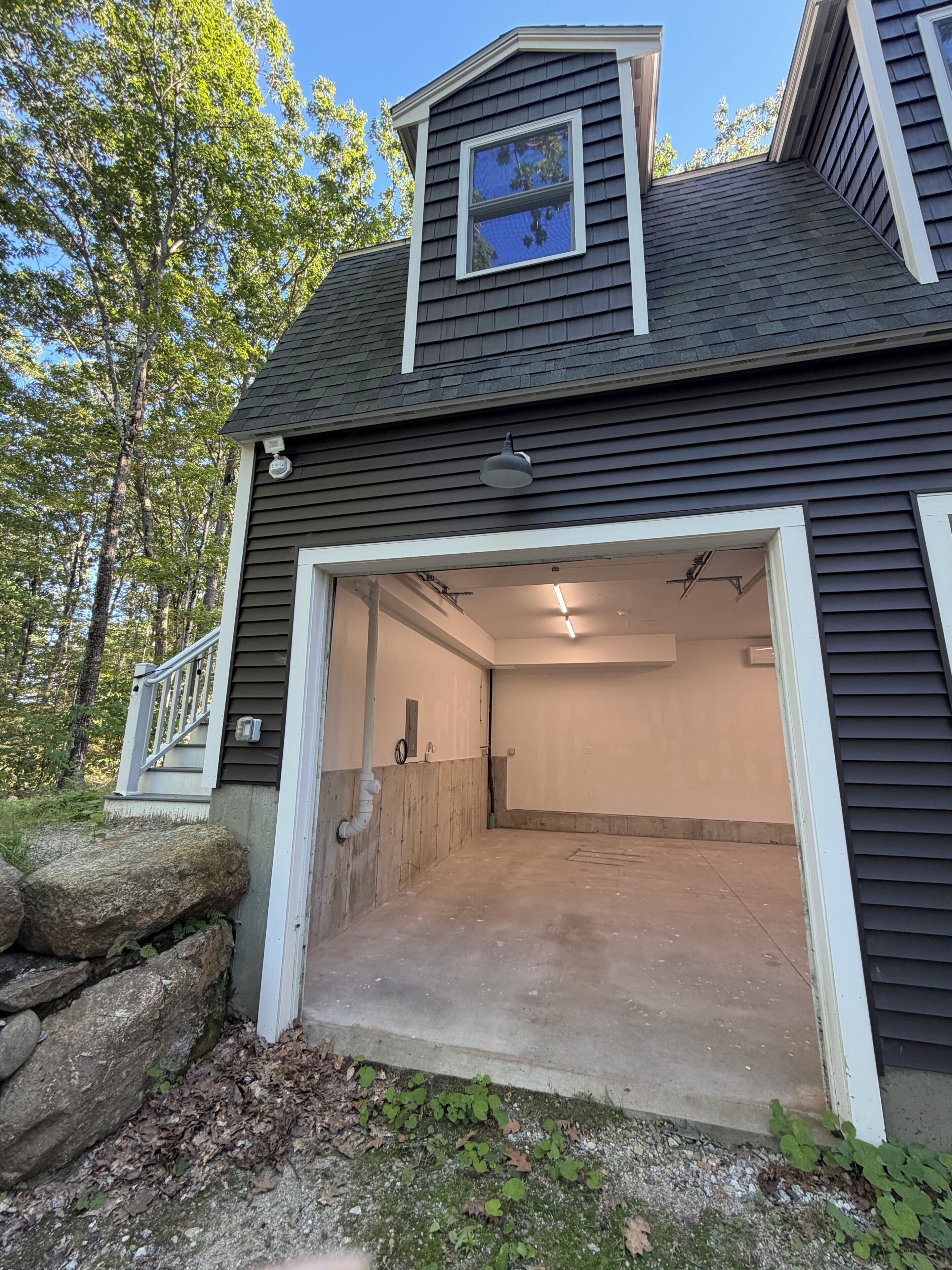 A house with a garage door open, a small porch, and a stone wall.