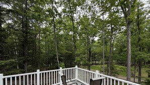 Terraza de madera con barandillas blancas, dos sillas y un bosque al fondo.