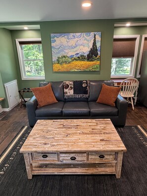 A living room with a black leather sofa, a painting above it, and a wooden coffee table in front.