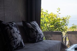 Ein Sofa mit gemusterten Kissen, Blick ins Grüne und ein Fenster.