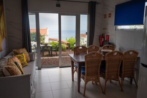 Ein Zimmer mit Essbereich, einer Couch mit Kissen und Meerblick durch große Glasfenster.