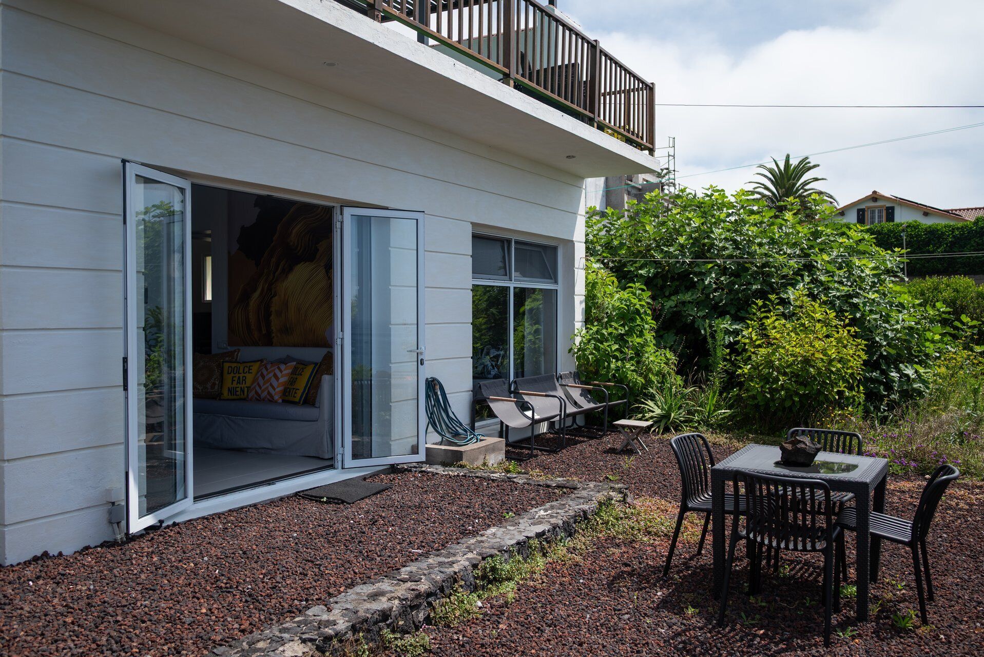 A modern house with a balcony, a patio with outdoor furniture, and a garden area.