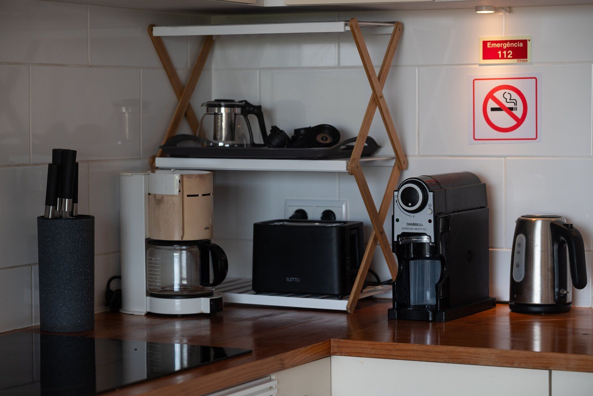 A kitchen with a coffee maker, toaster, kettle, and a no-smoking sign.