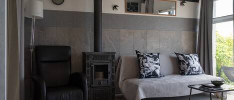 A modern living room with a black leather chair, a sofa with patterned cushions, a fireplace, and a large mirror on the wall.