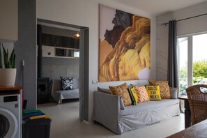 Ein modernes Wohnzimmer mit einem grauen Sofa, einem großen abstrakten Gemälde und Blick ins Grüne.