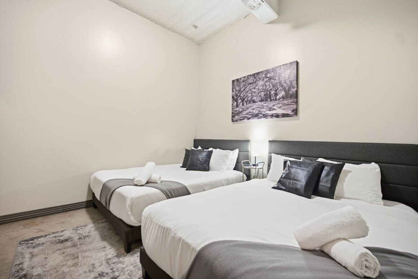 Habitación de hotel con dos camas, una mesita de noche, una lámpara y un cuadro en la pared.
