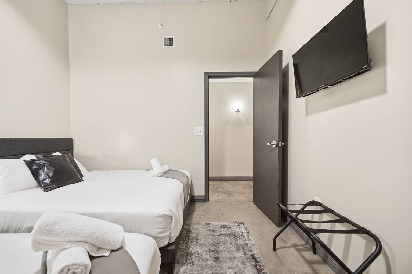 A hotel room with a bed, a TV mounted on the wall, and a door leading to another room.