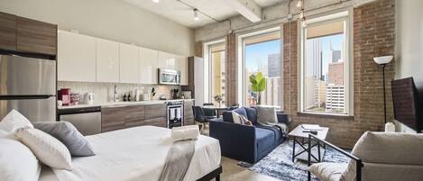 A modern apartment with a kitchenette, a bed, a sofa, and a dining area.