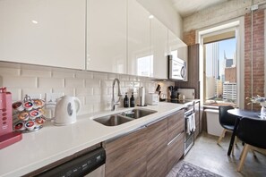 Eine moderne Küche mit weißen Schränken, Edelstahlgeräten und Blick auf die Stadt durch ein großes Fenster.