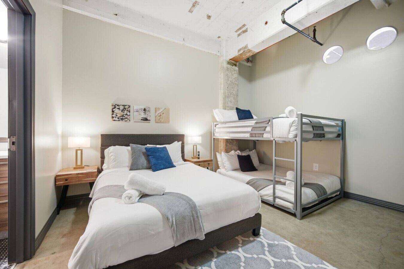 Een hotelkamer met een stapelbed, een eenpersoonsbed, een nachtkastje, een lamp en kunst aan de muur.
