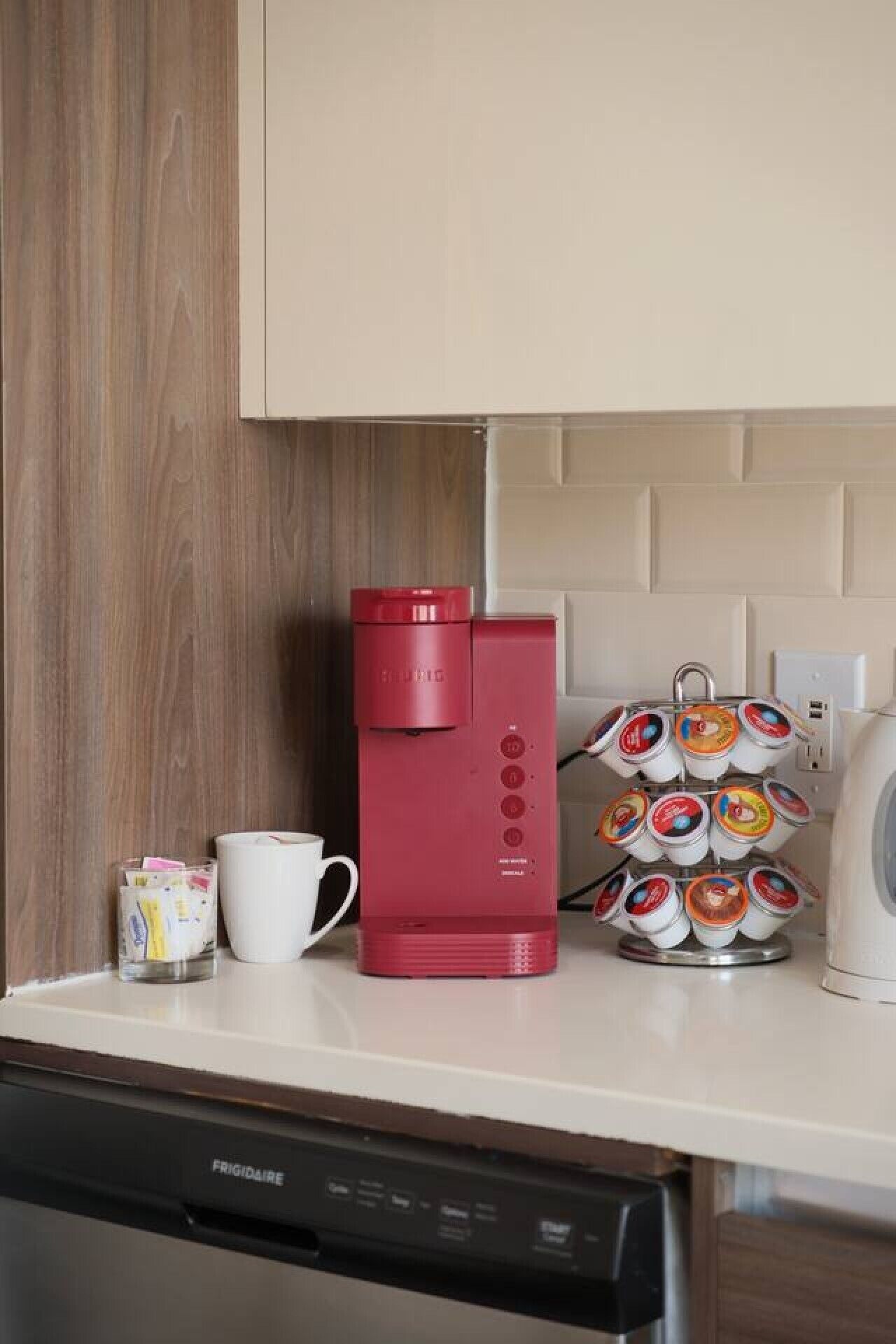 Een keukentafel met een rode koffiezetapparaat, een witte mok, een stapel koffiecups en een vaatwasser.