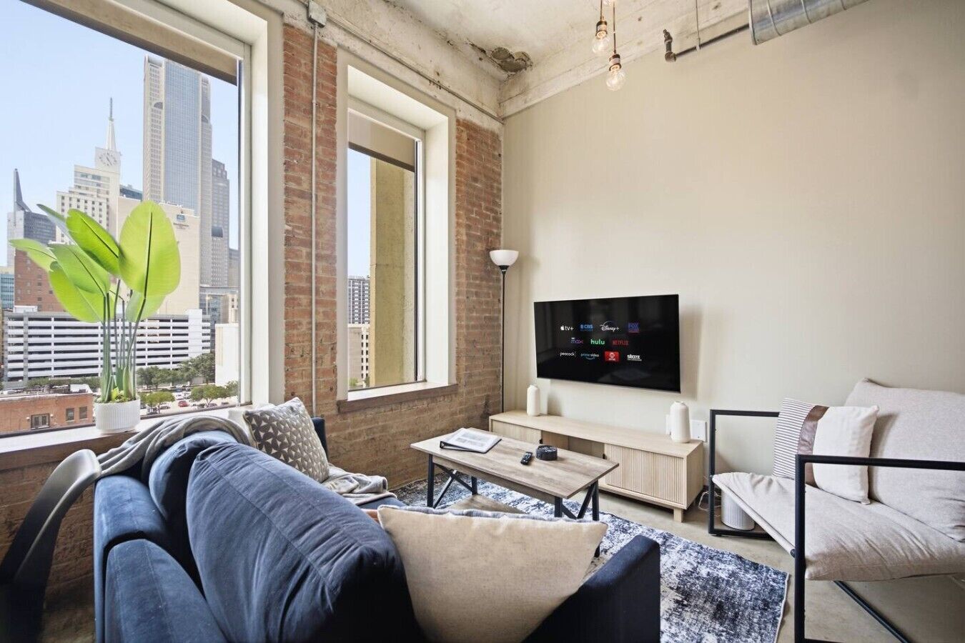 Un salon moderne doté d’une grande fenêtre, d’un téléviseur à écran plat et offrant une vue sur la ville.