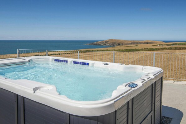 A hot tub with a clear view of the ocean and hills in the background.