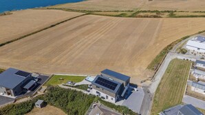 An aerial view of a residential area with fields, a body of water, and modern houses with solar panels. - Swn y Don, Gwbert - Six Bedroom Cottage, Sleeps 12 (Cardigan)