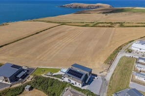 An aerial view of a residential area with fields, a body of water, and modern houses with solar panels. - Swn y Don, Gwbert - Six Bedroom Cottage, Sleeps 12 (Cardigan)