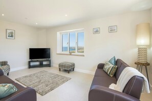 Neutral living room with two sofas, TV unit and window with sea view
