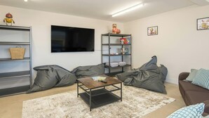 A living room with a flat-screen TV, a coffee table, grey bean bag chairs, a bookshelf, and a wall-mounted shelf. - Swn y Don, Gwbert - Six Bedroom Cottage, Sleeps 12 (Cardigan)