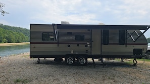 A Grey Wolf Limited RV parked on a gravel area by a body of water with trees in the background.