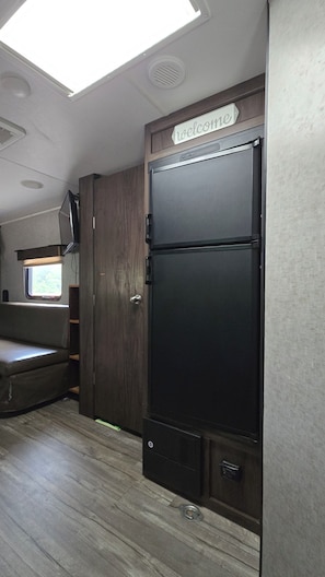 Un espacio kitchenette con un refrigerador negro, un armario de madera y una ventana con persianas.