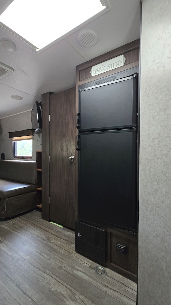 A compact kitchen area with a black refrigerator, a wooden cabinet, and a window with blinds.