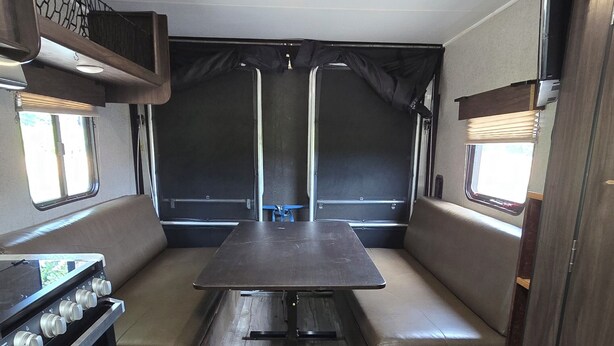 A compact RV interior with a kitchenette, seating area, and a table. - Cozy Camper on Current River - Private Boat Ramp with a Dock and Views. (Doniphan)