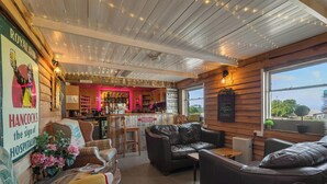 A cozy bar area with wooden walls and a bar counter, featuring a variety of bottles and a menu board.