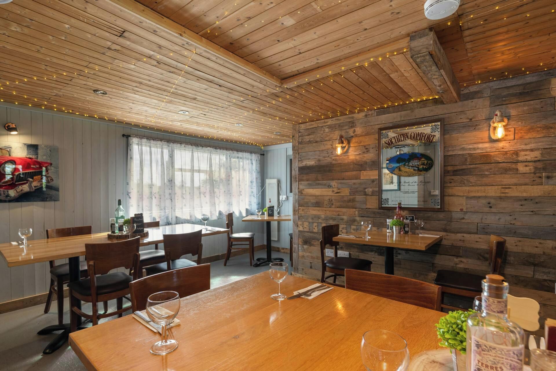 L’intérieur d’un restaurant avec des plafonds en bois, des guirlandes lumineuses et une grande fenêtre ornée de rideaux.