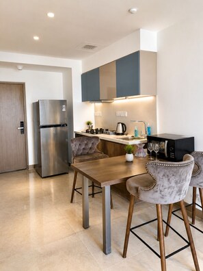 A modern kitchen with a stainless steel refrigerator, a dining table with chairs, and a microwave.