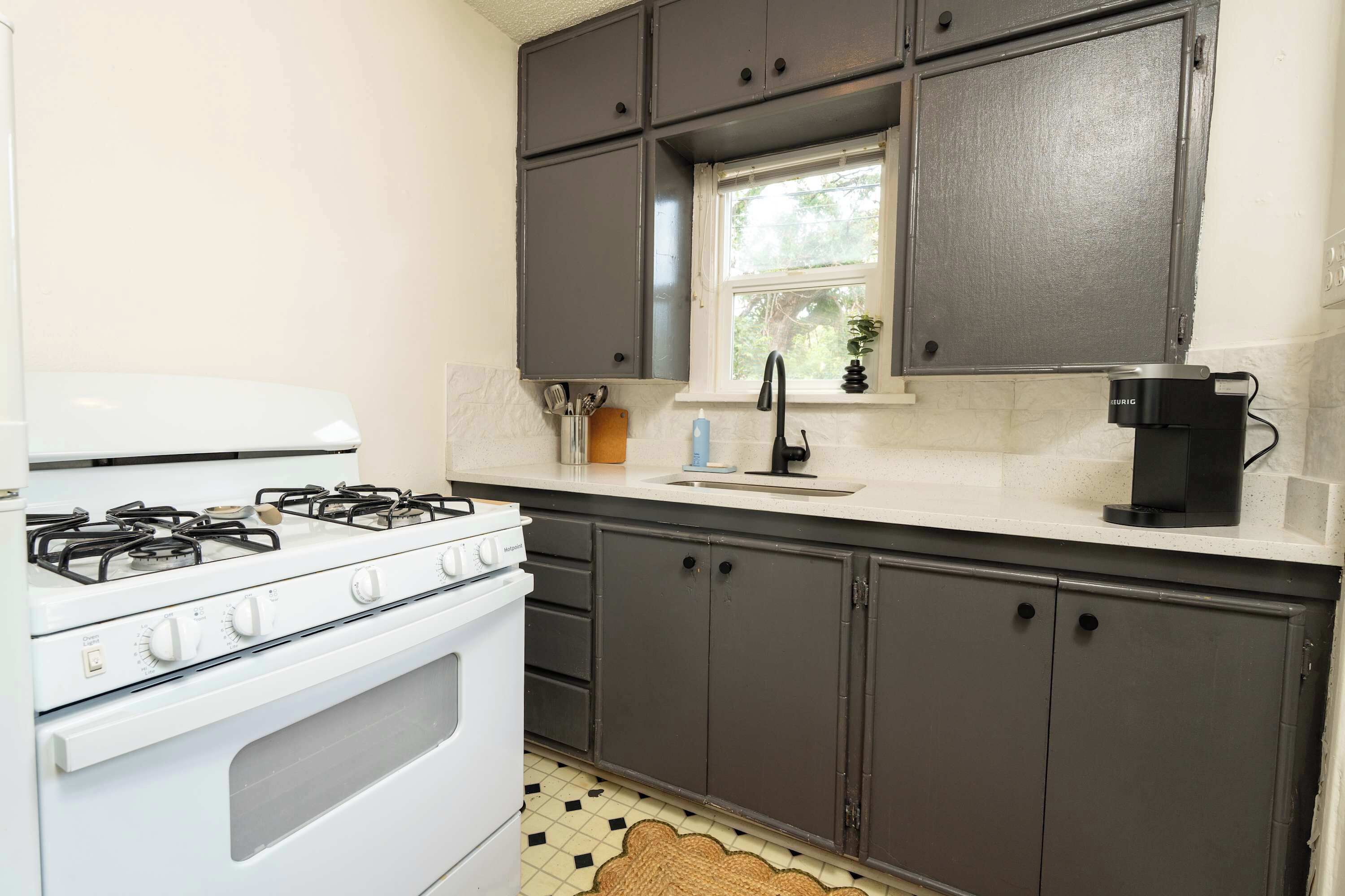 A kitchen with a white stove, dark cabinets, a window, and a coffee maker.