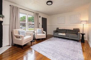 A living room with two armchairs, a sofa, a coffee table, and a rug. There are two windows with curtains, a door, and wall art. - Beautiful One Bedroom Located Near Golf course (Wichita)