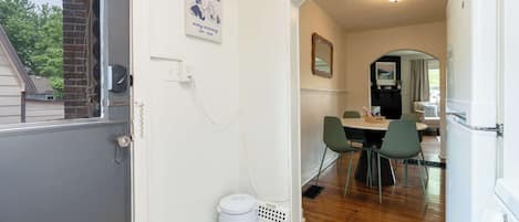 A narrow hallway leading to a dining area with a table and chairs, a trash can, and a refrigerator.