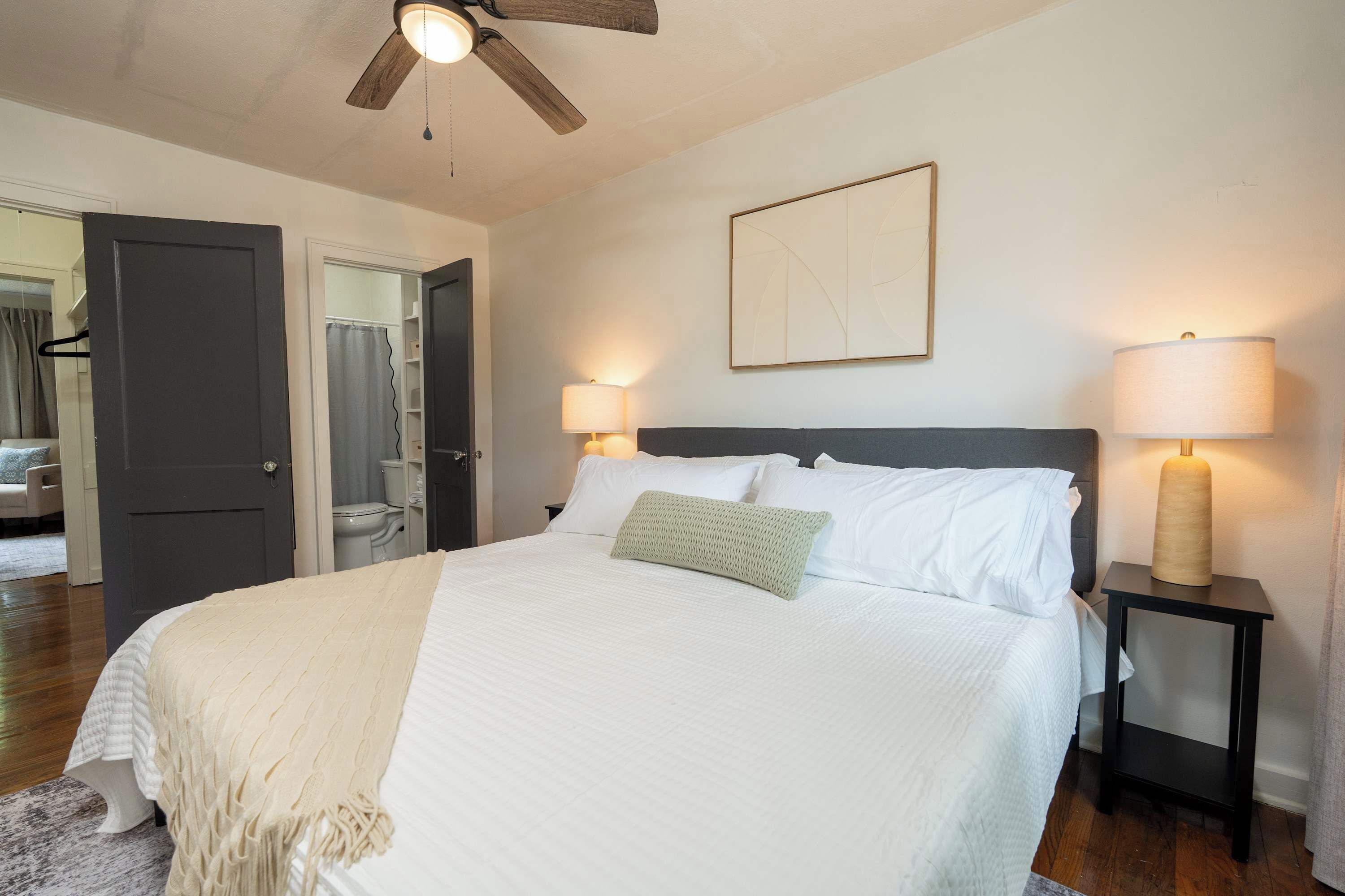 A bedroom with a bed, bedside lamps, a ceiling fan, and a painting on the wall.