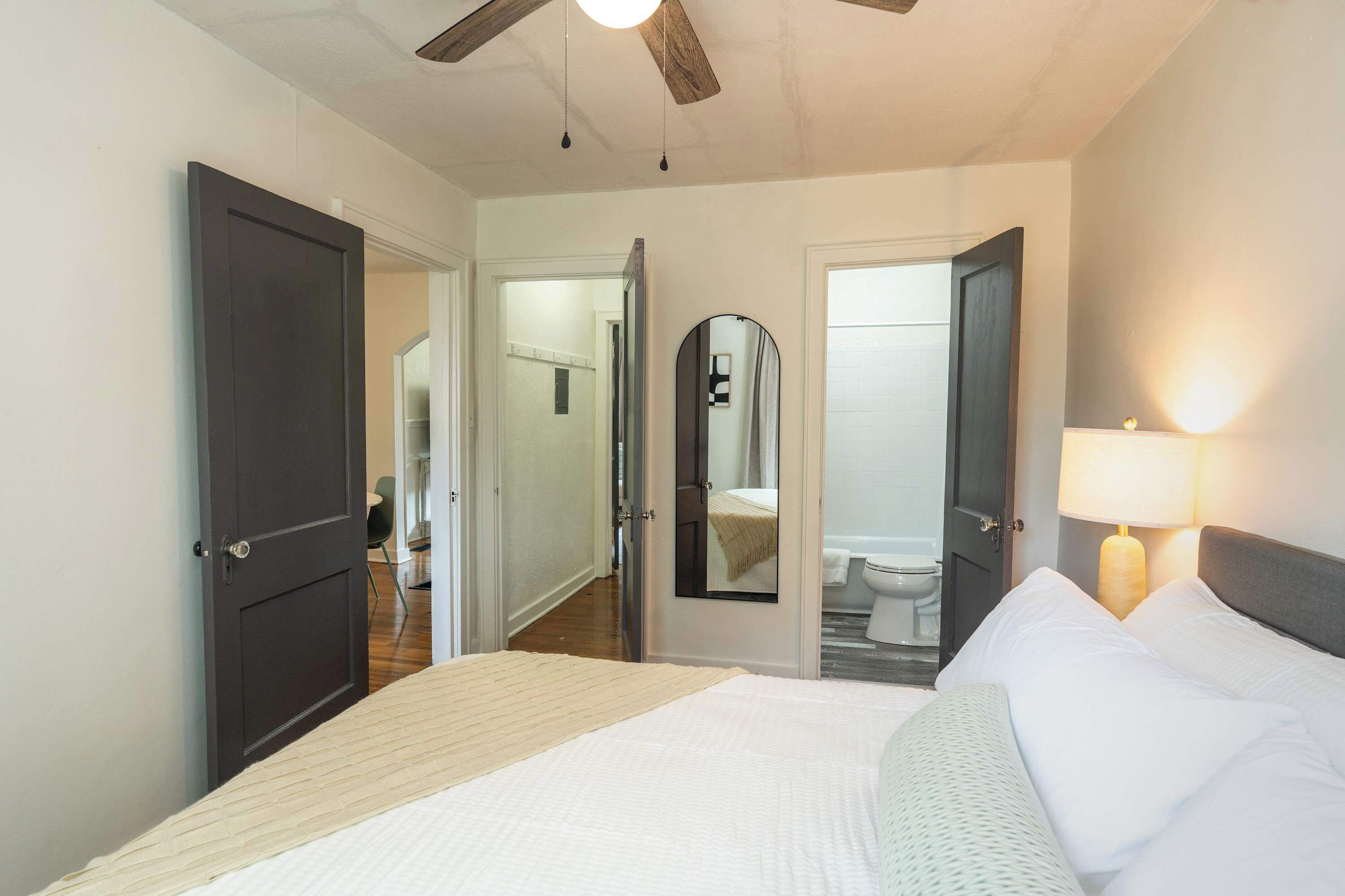 A hotel room with a bed, a bedside lamp, a ceiling fan, and a bathroom visible through an open door.