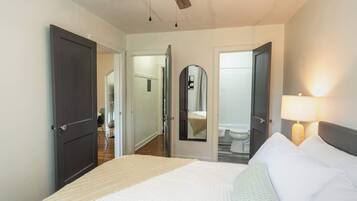 A hotel room with a bed, a bedside lamp, a ceiling fan, and a bathroom visible through an open door.