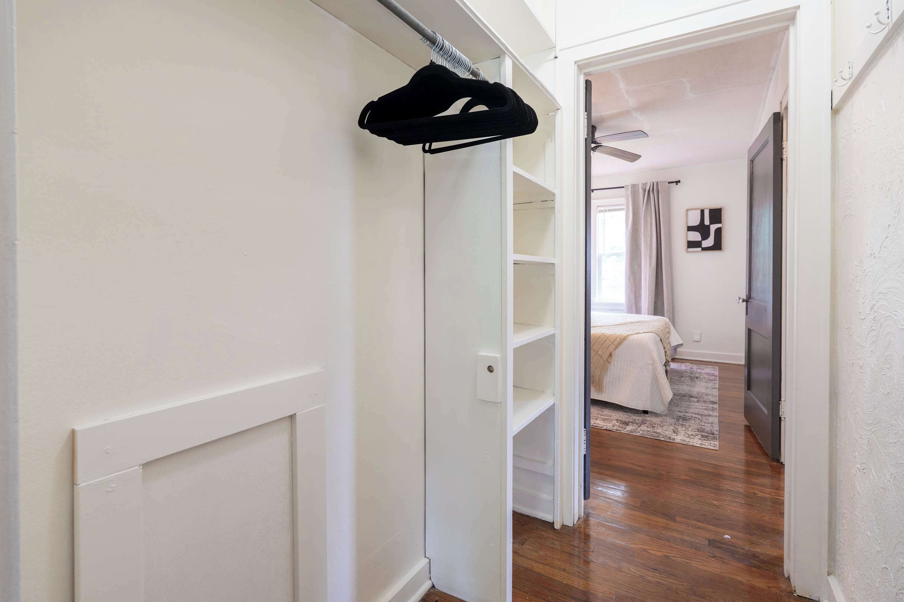 A hallway leading to a bedroom with a bed, a window with curtains, and a hanging garment.