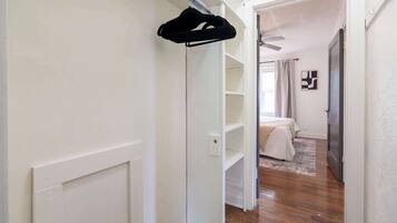 A hallway leading to a bedroom with a bed, a window with curtains, and a hanging garment.